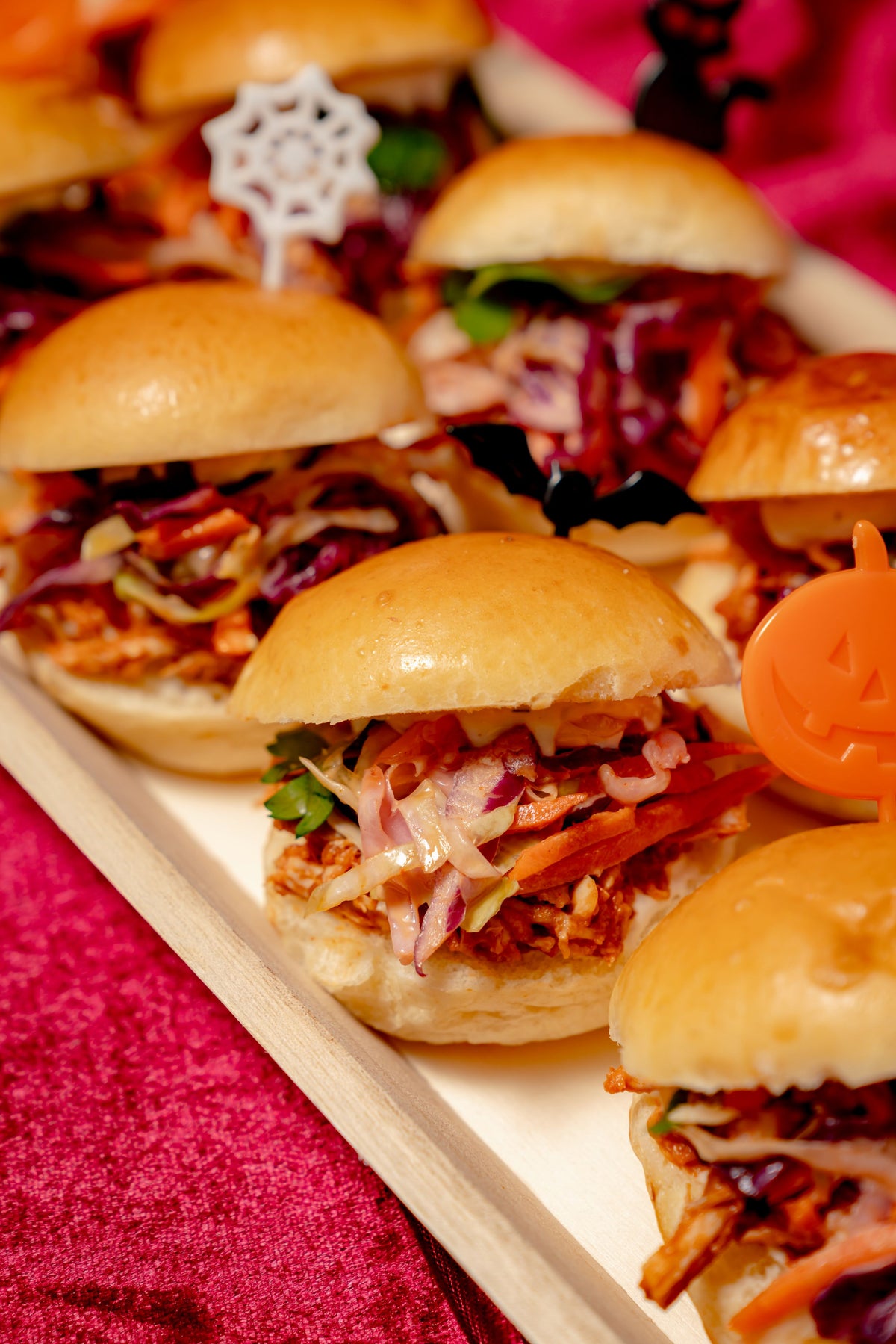 A platter of BOOfalo Chicken Monster Sliders topped with tricolor slaw and adorned with decorative Halloween-themed food picks.