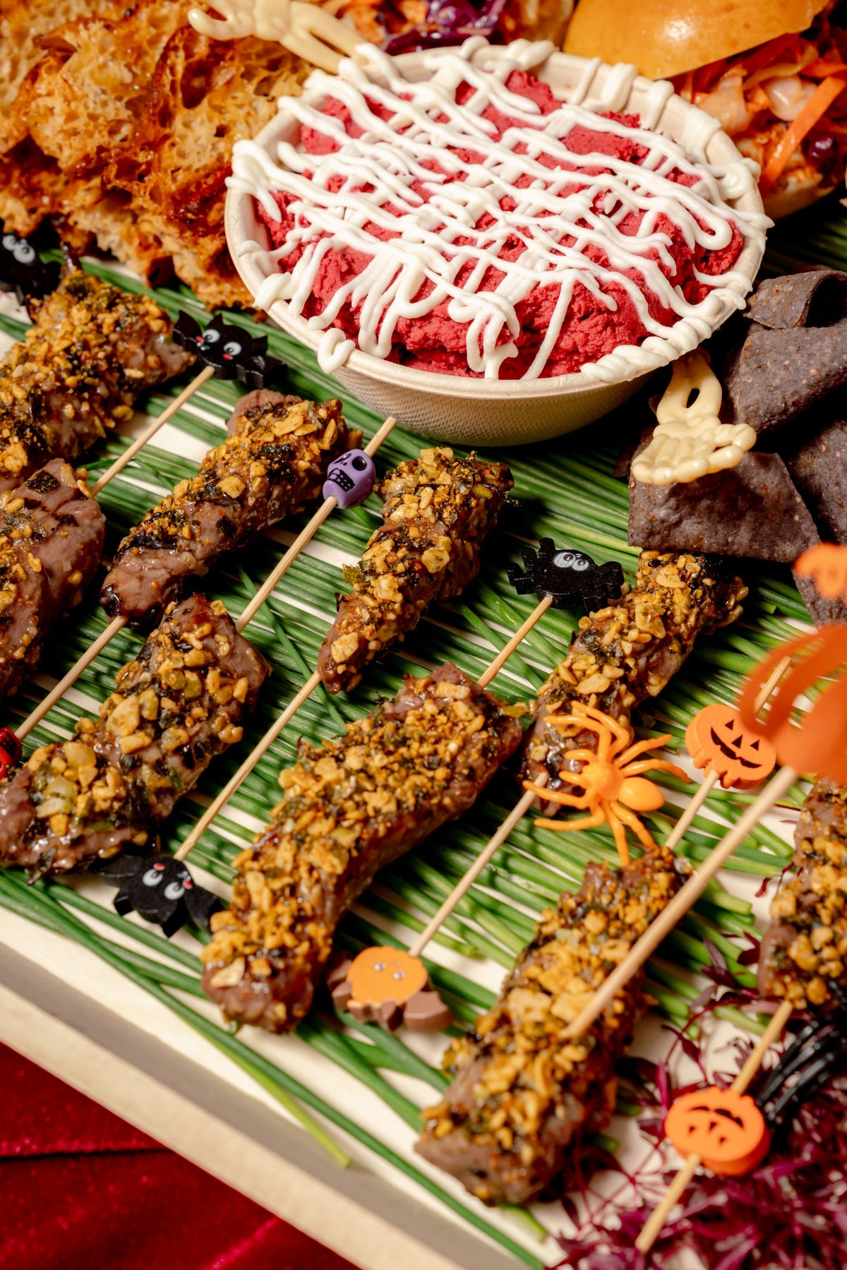 Halloween Savory Platter featuring herb-crusted beef skewers, beet dip with cream, and tortilla chips, decorated with small plastic Halloween-themed figures.