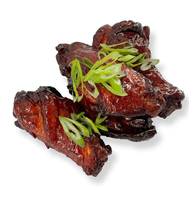 Three Chipotle BBQ Wings glazed with maple syrup and topped with sliced green onions on a white background.