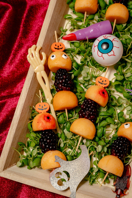 Lurch’s Fruit Skewer Eyes featuring cantaloupe balls and blackberries, decorated with small pumpkin and eyeball toppers on a bed of microgreens.