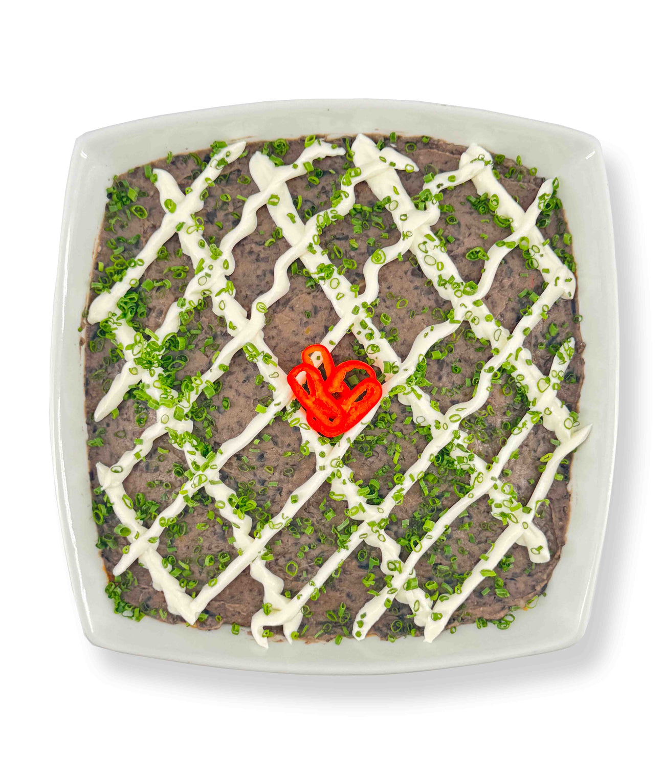 A square dish of 6 Layer Dip topped with Whitestone Cheddar, a mayonnaise drizzle, green onions, and a red chili pepper slice in the center. Serve with guacamole and corn tortillas for a complete flavor experience.