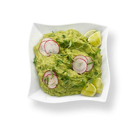 Vegetable Crudite with Guacamole in a square white dish, garnished with radish slices, fresh cilantro, microgreens, and lime wedges on a pristine white background.