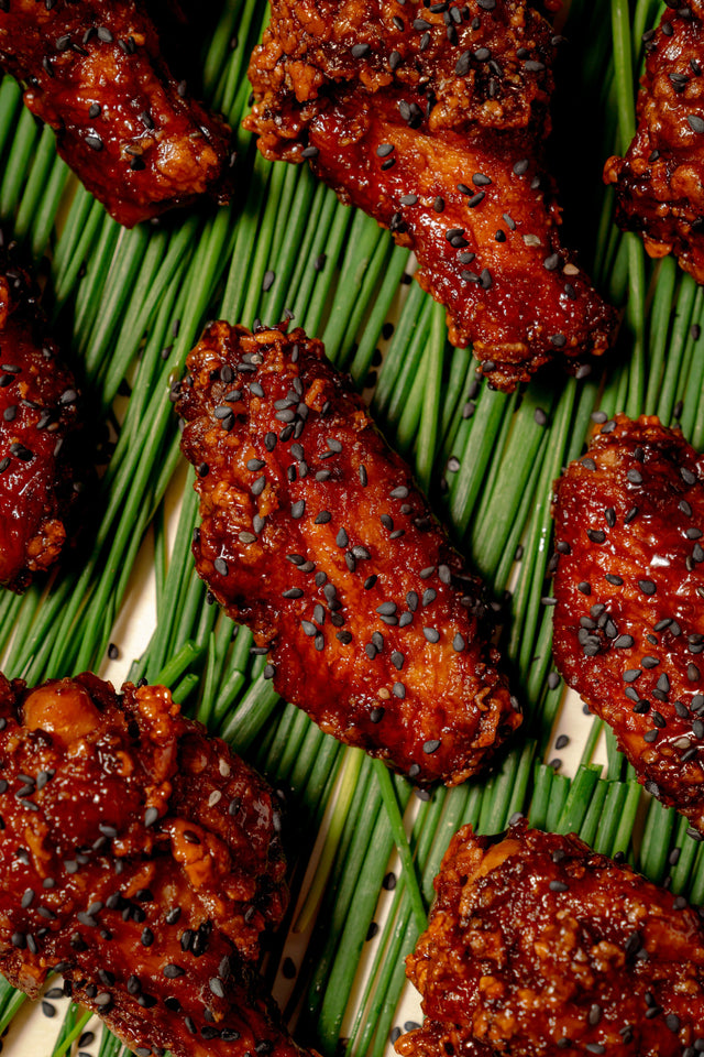 Bat Wings: Asian-glazed, crispy chicken wings with black garlic, sprinkled with black sesame seeds and arranged on a bed of fresh chives.