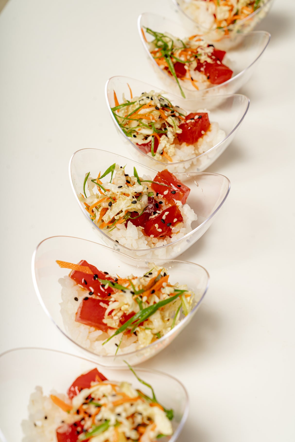 Six Mini Tuna Poke Bowls arranged diagonally, each filled with sushi rice, diced tuna, shredded vegetables, and topped with sesame seeds, green onions, and a citrus lemongrass ponzu drizzle.
