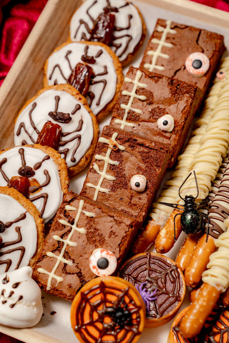 The Haunted Bake Shop Platter featuring frosted spider cookies, stitch-decorated brownies with candy eyes, chocolate-drizzled pretzel rods, and spiderweb-topped cookies.