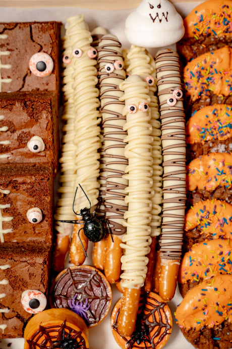The Haunted Bake Shop Platter containing chocolate brownies with candy eyes, white chocolate mummy pretzel rods, and pumpkin spice cookies with orange frosting, sprinkles, and spiders.