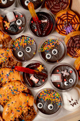 The Haunted Bake Shop Platter features pudding cups with candy eyes and gummy worms, alongside frosted pumpkin spice cookies decorated with spiderwebs and orange icing.
