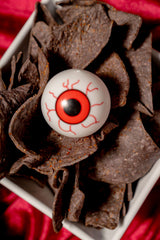 6 Feet Deep Graveyard Dip Platter featuring a white square bowl filled with black tortilla chips, topped with a plastic eyeball.