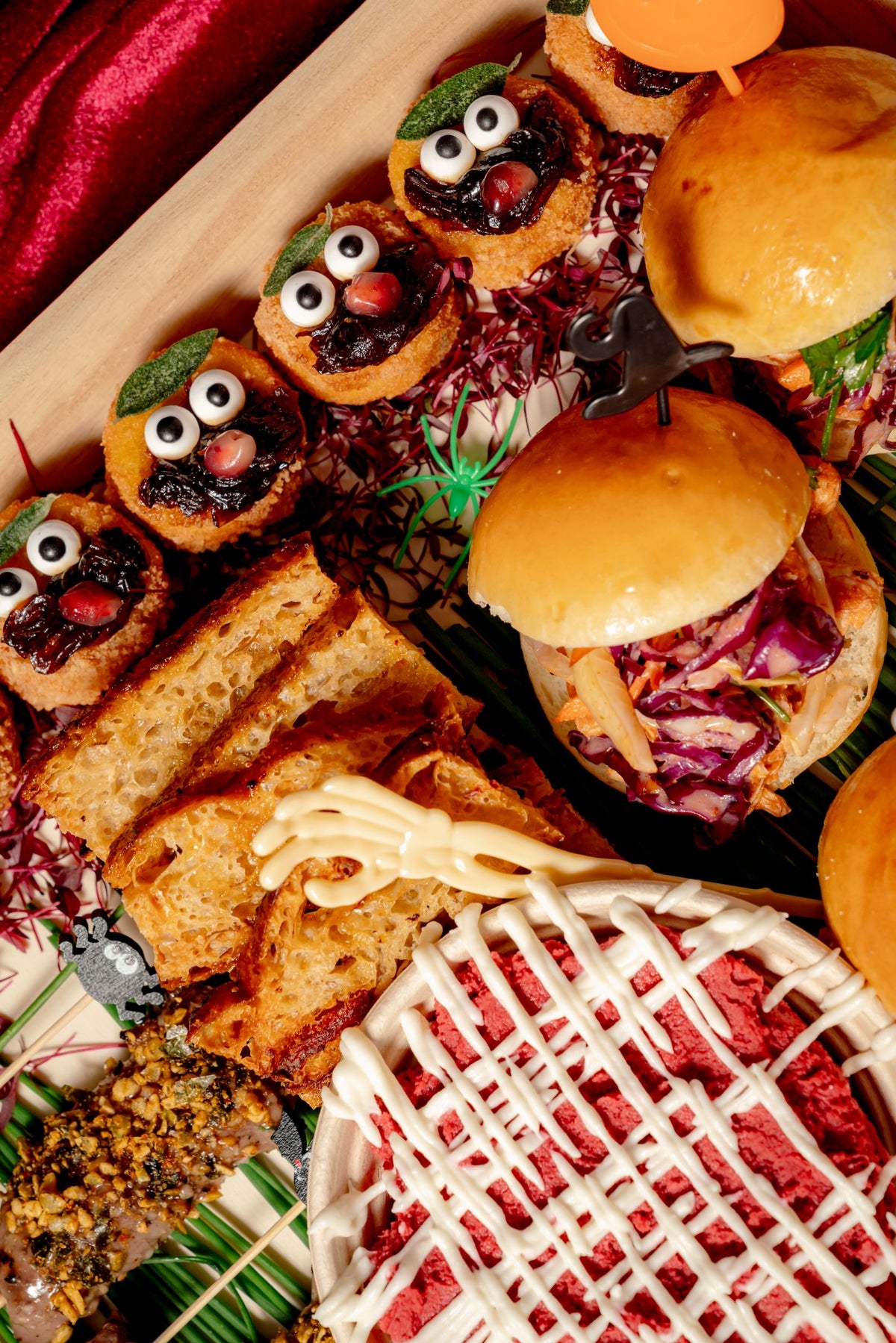 Haunted Grazing Platter on a wooden tray featuring sliders, toasted bread, and small bites decorated with edible googly eyes and a plastic skeleton hand.