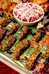 Halloween Savory Platter featuring herb-crusted beef skewers, beet dip with cream, and tortilla chips, decorated with small plastic Halloween-themed figures.