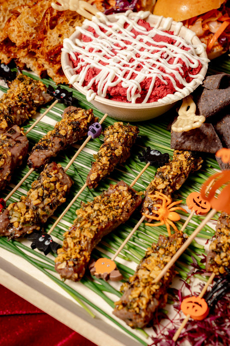 Halloween Savory Platter featuring herb-crusted beef skewers, beet dip with cream, and tortilla chips, decorated with small plastic Halloween-themed figures.