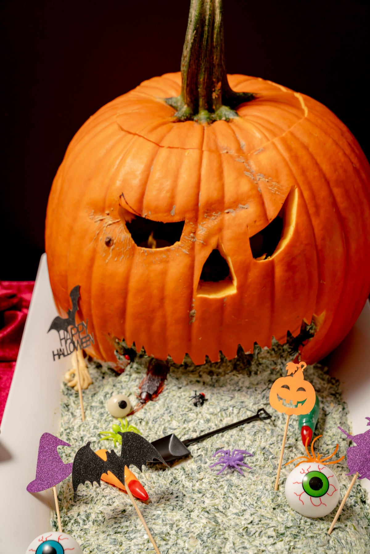 A Puking Pumpkin Platter features a carved pumpkin on a white tray with spinach dip spilling from its mouth over black tortilla chips, plastic eyeballs, spiders, and bats on picks.