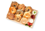 The Homemade Bagels & Spreads set features nine assorted bagels on a wooden tray, served with three small containers of cream cheese and jam, plus strawberry slices on the side.