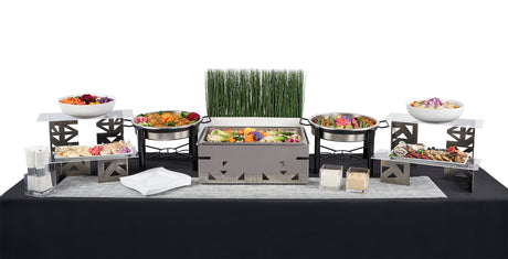 The Double Entree Package showcases a delightful buffet with salads, vegetables, breads, cheeses, various sides and proteins, and includes serving dishes, plates, decorative greenery on a black and white tablecloth.