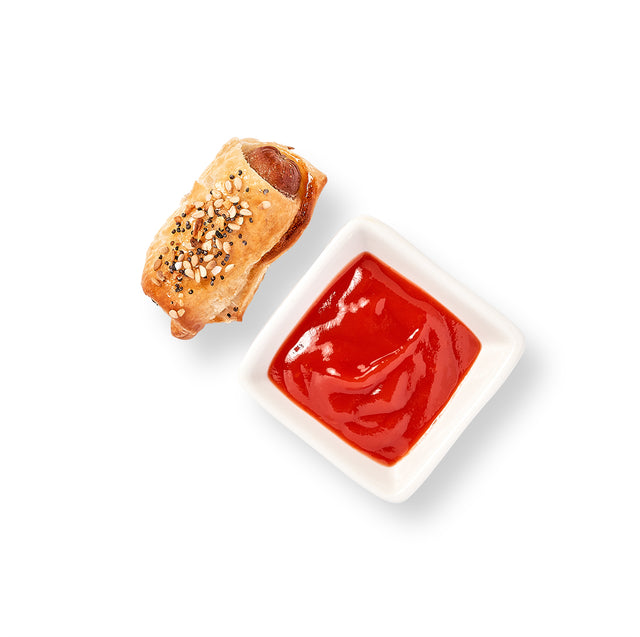 A Mini Beef Frankfurter with ketchup and stone ground mustard on a plate.
