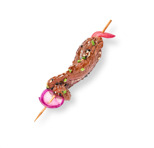 A Sesame Beef Skewer with meat and onions on it, accompanied by an Orange Ginger Dipping Sauce.