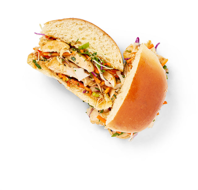 A Chicken Bahn Mi sandwich is cut in half on a white background.